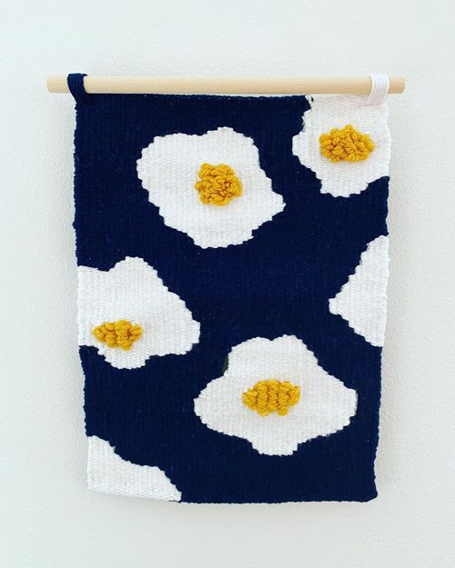 A tapestry of fried eggs on a navy background. The yolks are puffy, made of rya loops.