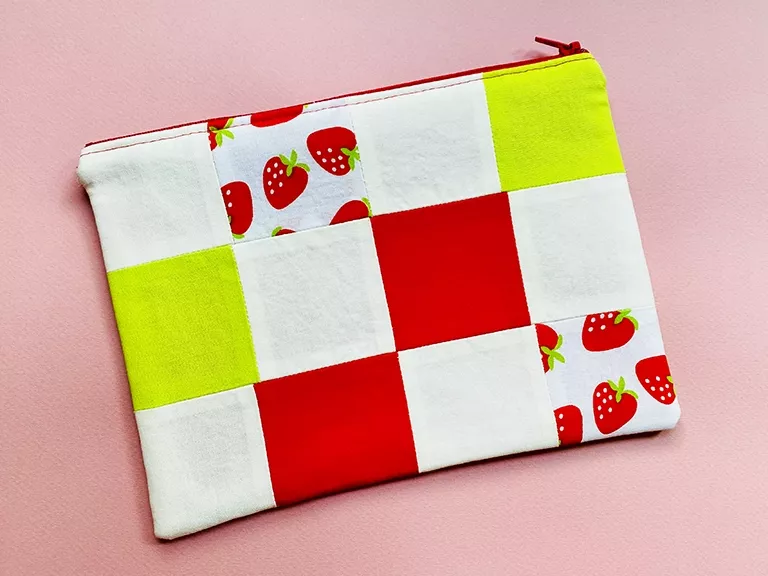 A checkerboard pattern of squares in the following fabric colors: cream, red, lime green, and a printed pattern of red strawberries on a white background. Their stems are lime green