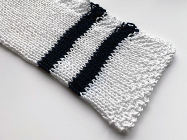 A white knitted washcloth with two thick navy bands near one edge