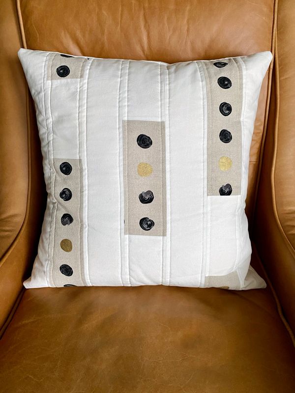 The quilted pillow with cream and dot-patterned stripes, resting against the back of a brown leather chair.