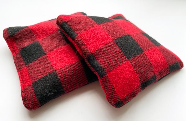 Two poofy, five-inch square sachets made out of black and red plaid flannel fabric
