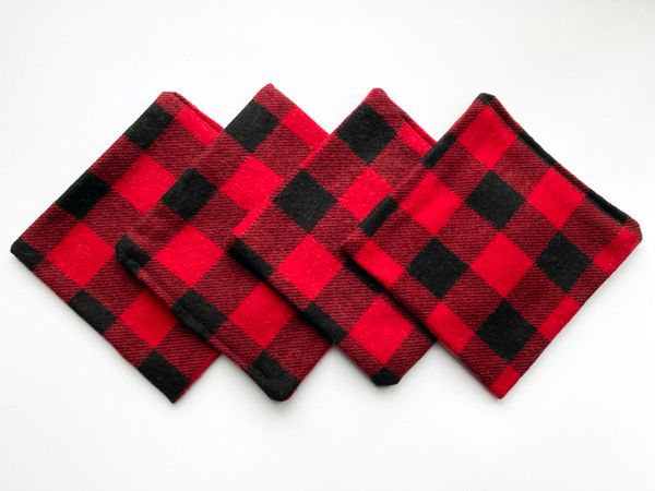 A set of four, square coasters made out of black and red plaid flannel fabric