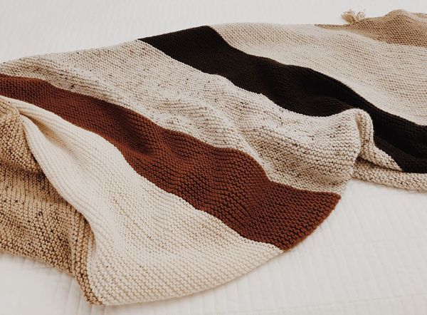 A knitted blanket in neutral earth tones, in large stripes along the bias