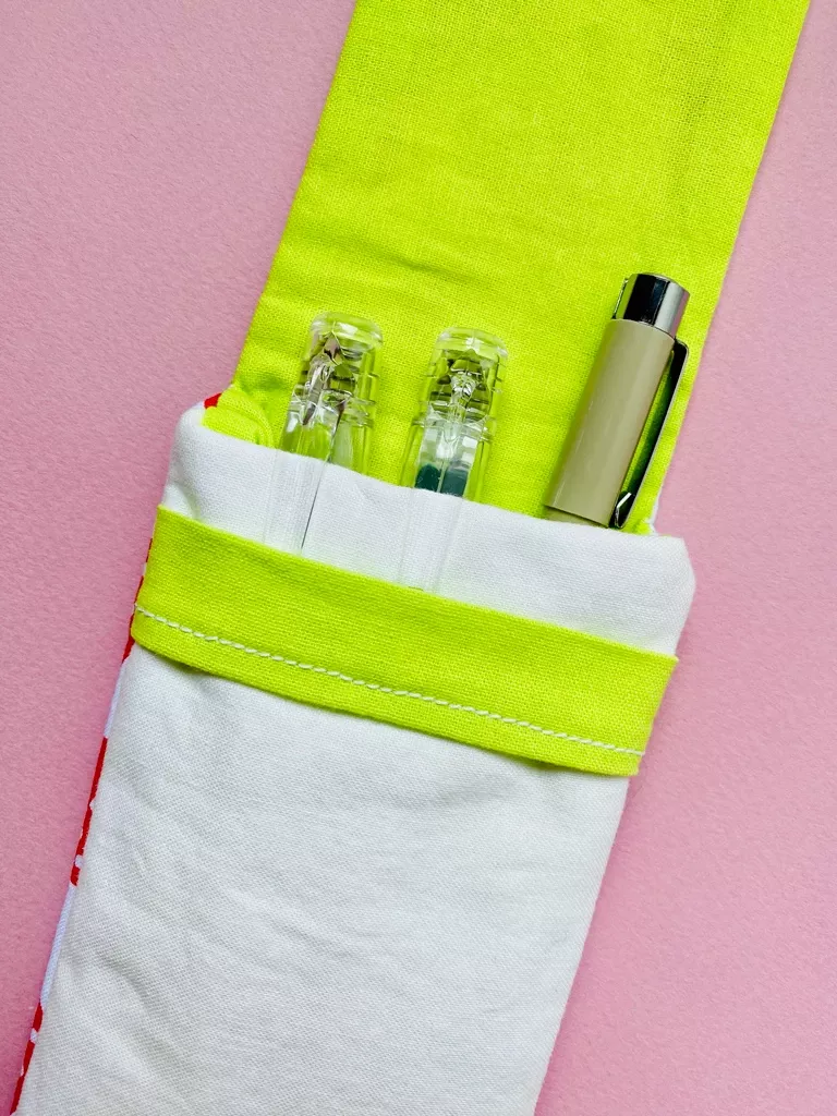 The pouch is open to show 3 pens inside. The lining fabric is bright green, juxtaposed against a secondary outer fabric which is cream.