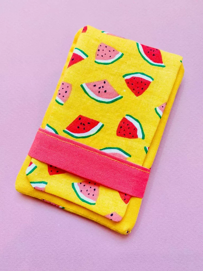 A fabric pouch made from solid yellow fabric and a yellow fabric with a pink and red watermelon pattern. A pink strap runs one inch from the bottom.